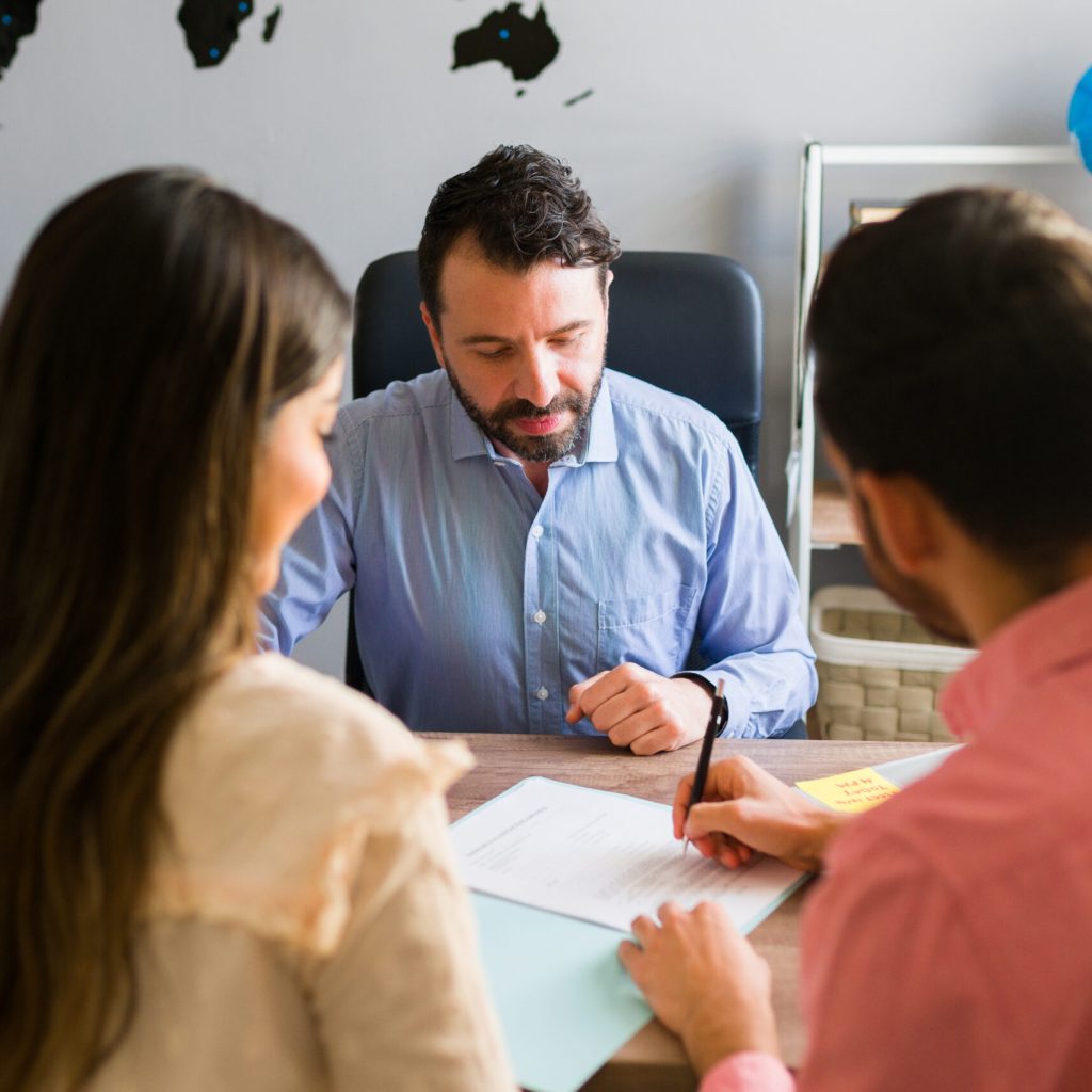 You got a deal. Young man signing a sales contract for a holiday vacation with his wife. Sales representative closing a deal for a timeshare sale with some customers at the travel agency